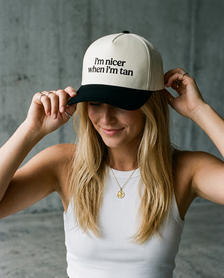 Woman wearing a cap with text, standing against a gray concrete wall.