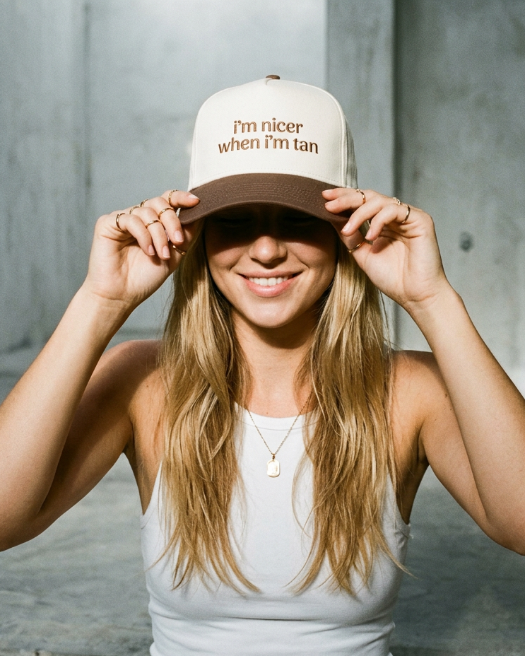 Woman wearing a cap with text, standing against a concrete wall.