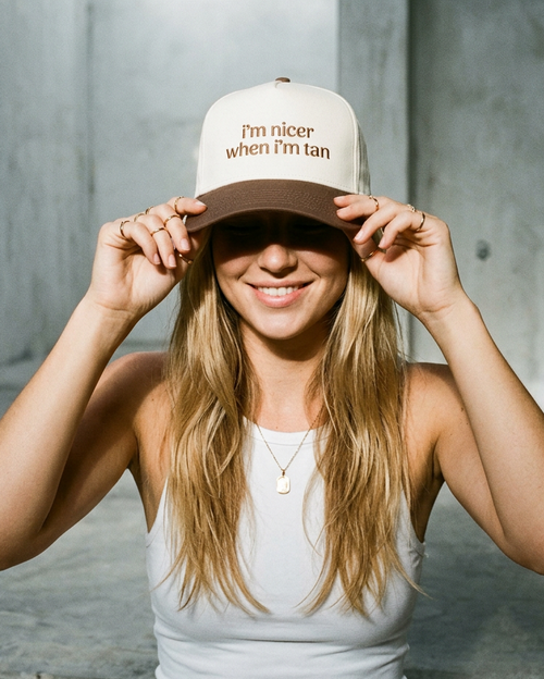 Woman wearing a cap with text, standing against a concrete wall.