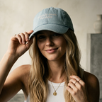 Woman wearing a light blue denim cap with text, standing against a neutral background