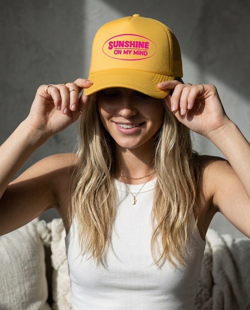 Woman wearing a yellow cap with 'Sunshine on My Mind' text, smiling against a neutral background