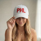Woman wearing a white cap with 'PHL' in red on a neutral background