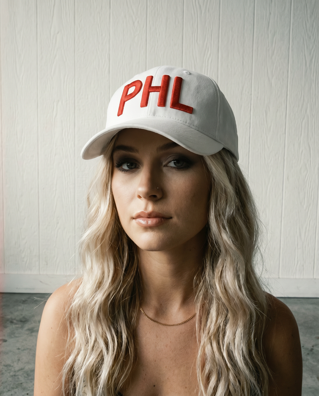 Woman wearing a white cap with 'PHL' in red on a light wooden background