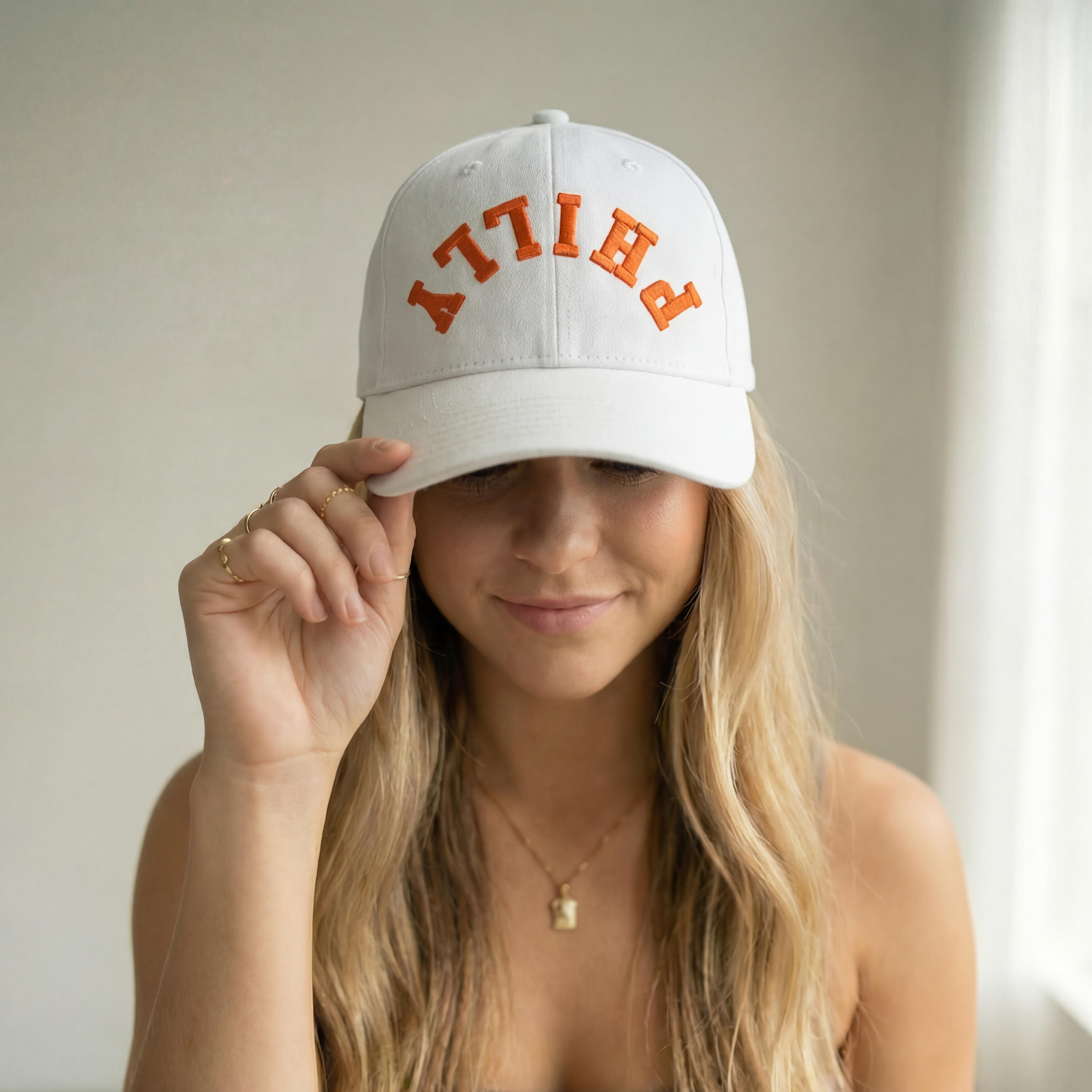 Woman wearing a white cap with 'PHILLY' embroidered in orange on a neutral background