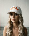 Woman wearing a white cap with 'Philly' in orange on a light wooden background